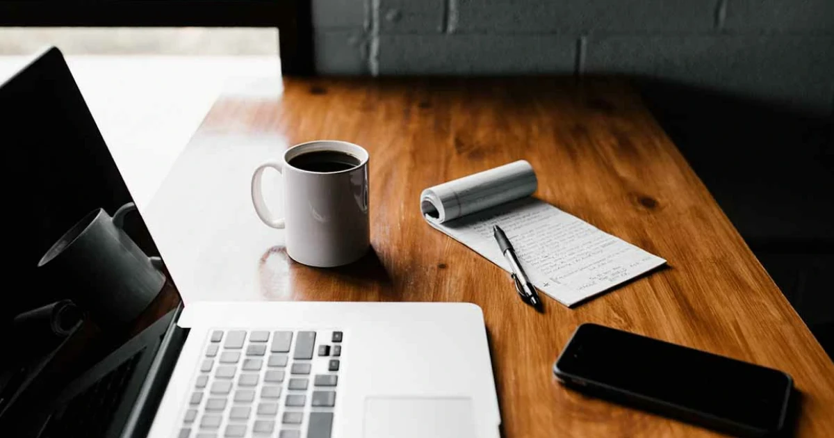 a cup of coffee, a notepad, and laptop on a desk