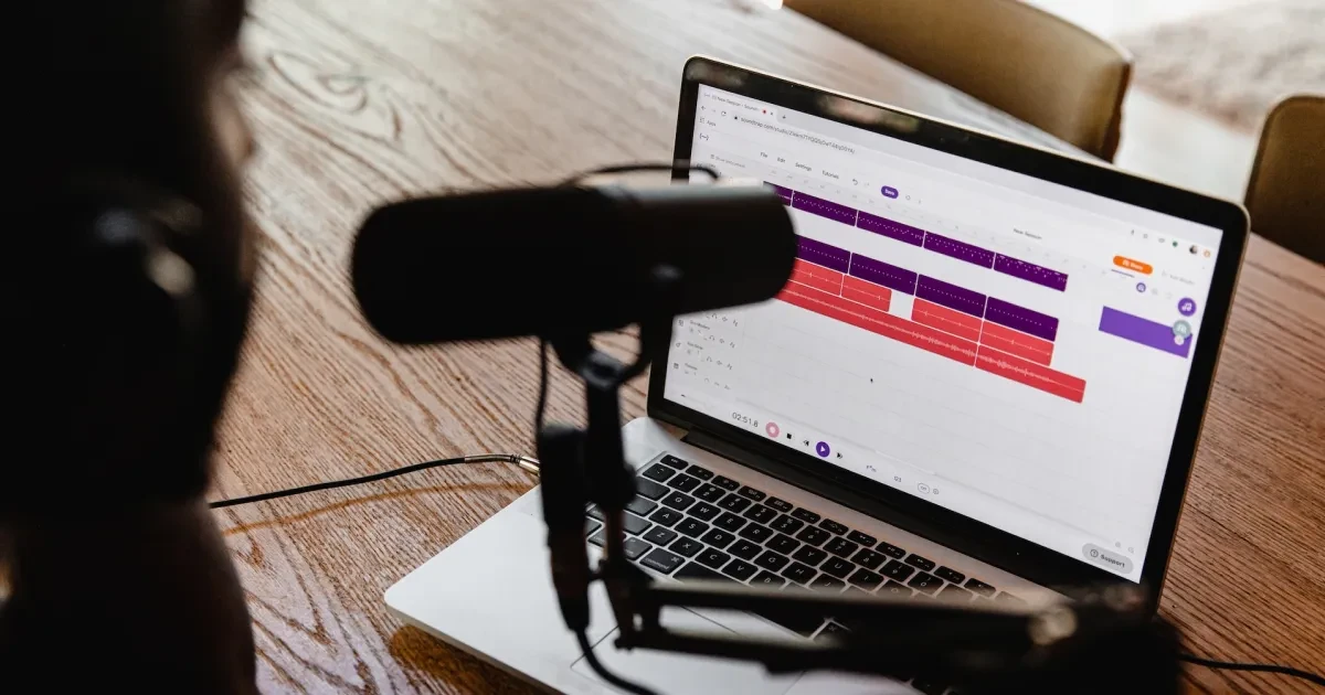 a person in front of a mic and a laptop wearing headphones